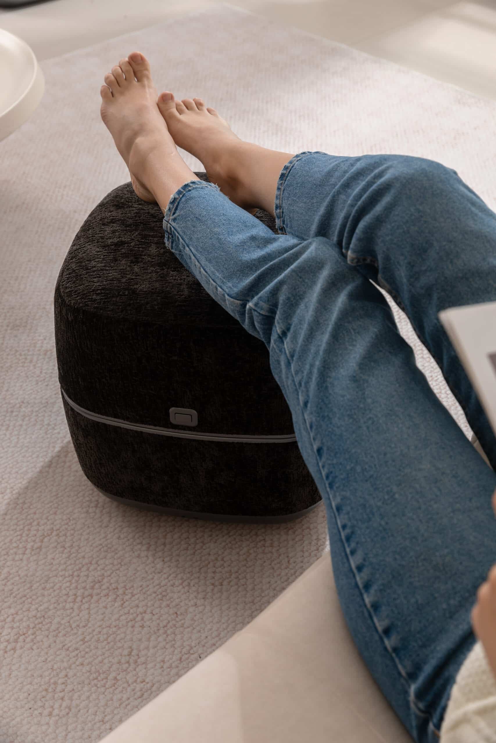 Person vilar fötterna på en svart fotmassageapparat med mjuk textil och modern design